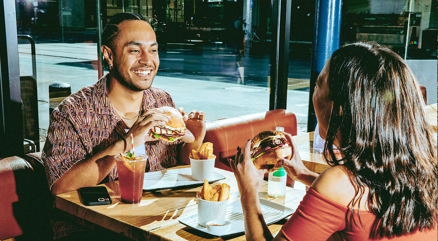A man and woman enjoy cheeseburgers and fries together at a cozy restaurant table.